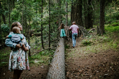 Father helping daughter walk on log while mom watches