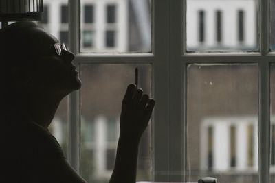 Side view of woman smoking cigarette against glass window