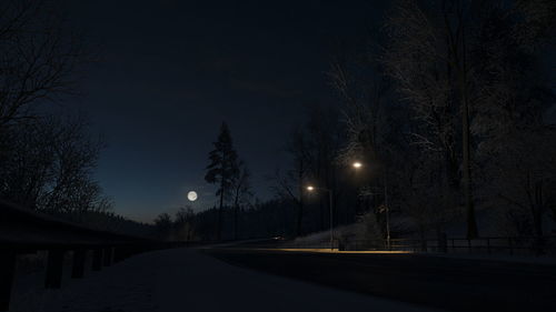 Illuminated street lights on road against sky at night