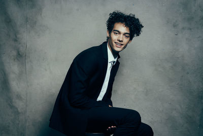 Portrait of young man sitting against wall