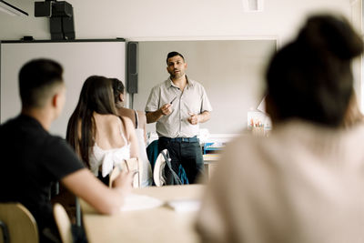 Professor teaching while teenage students sitting in classroom