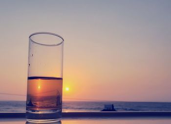 Close-up of beer glass against sea during sunset
