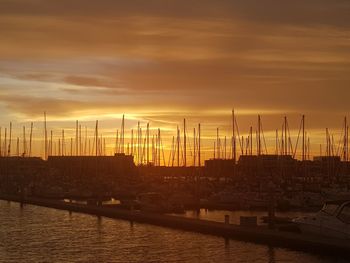 Sailboats moored in harbor against orange sky