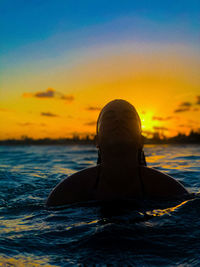 Silhouette man swimming in sea against sunset sky