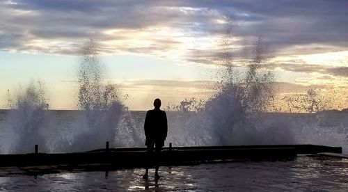 Rear view of silhouette man standing by swimming pool against sky