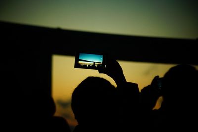 Silhouette people photographing illuminated smart phone