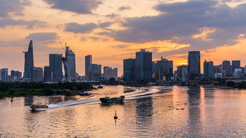 Sea by modern buildings against sky during sunset