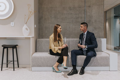 Full length of male and female delegates sitting on sofa discussing during seminar