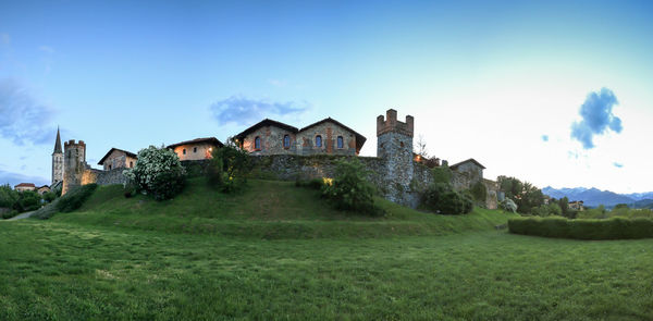 Houses on grassy field against cloudy sky