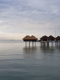 Stilt house by sea against sky during sunset