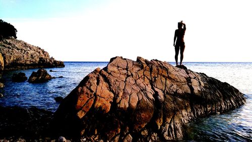 Silhouette woman on rock by sea against clear sky