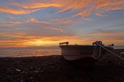 Boat moored on beach against cloudy sky during sunset