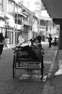 Man sitting on footpath against buildings in city