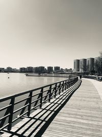 Footpath by lake against buildings in city against clear sky