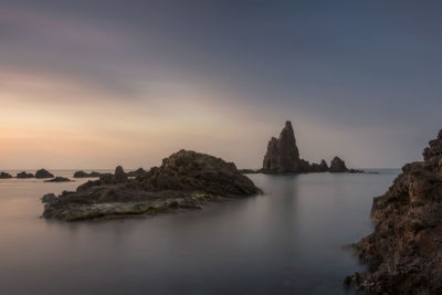 Rock formation in sea against sky during sunset