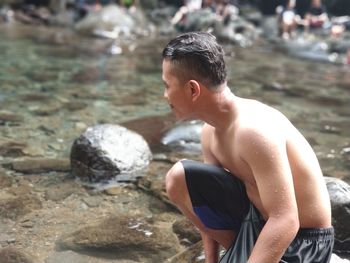 Side view of shirtless man crouching in river