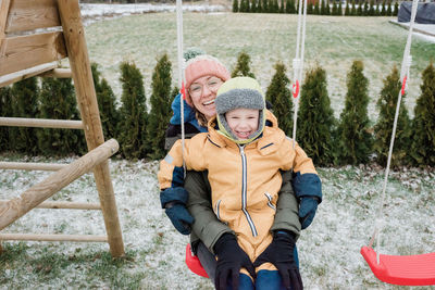 Son sitting on mothers lap whilst swinging outside in the snow