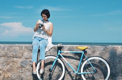 Young woman using phone while standing by sea against sky