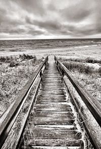Boardwalk leading towards sea against sky