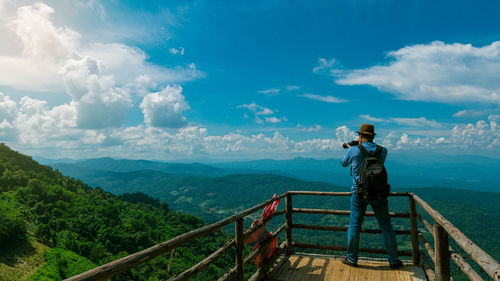 Rear view of man standing on railing against mountain