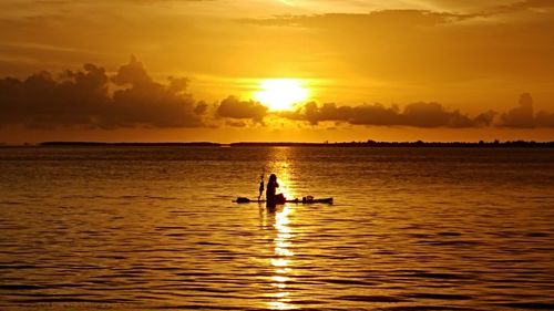 Silhouette woman paddleboarding on sea against sky during sunset