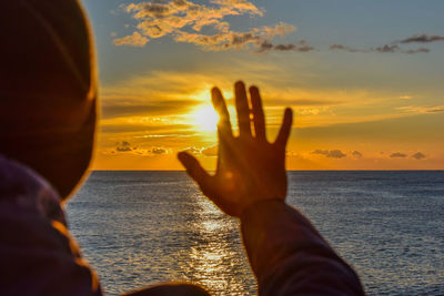 Man gesturing stop sign at beach against sky during sunset