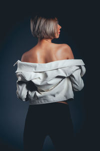 Rear view of seductive woman wearing jacket standing against black background