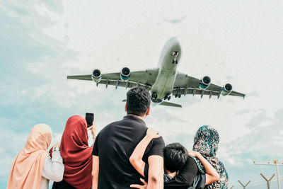 Rear view of family looking at airplane flying against sky