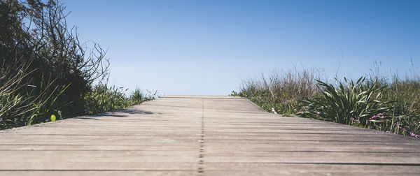 Close up view of wooden walkway leading to the sea through low mediterranean vegetation path of wood