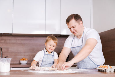 Happy smiling caucasian family in aprons cooking and kneading dough on a wooden