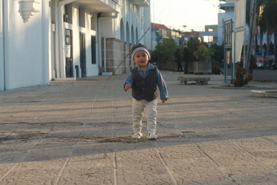 Full length of cute baby boy standing on street against buildings