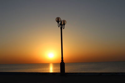 Silhouette street light by sea against sky during sunset