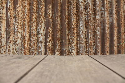 Close-up of wooden table against rusty metallic wall