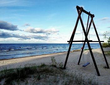 Swing at calm beach against blue sky