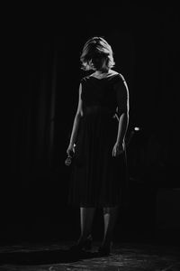 Portrait of woman standing against black background