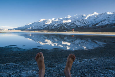 Low section of person on snowcapped mountains by lake