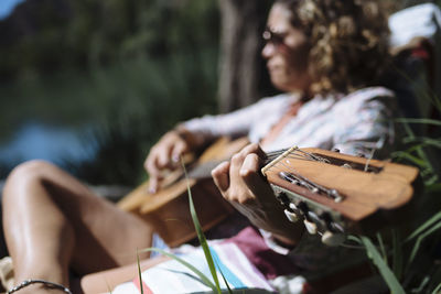 Woman with sunglasses playing guitar lying on a hammock.