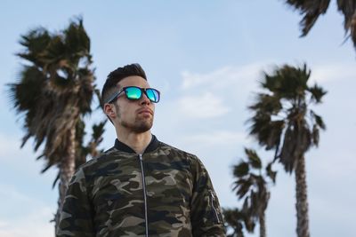 Thoughtful man looking away while standing against sky