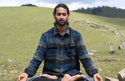 A young indian guy practicing meditation, yoga in lotus pose, padmasana in the mountain.