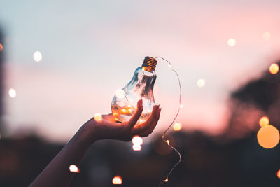 Close-up of woman holding illuminated lighting equipment against sky at night