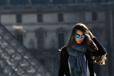 Portrait of young woman standing against building