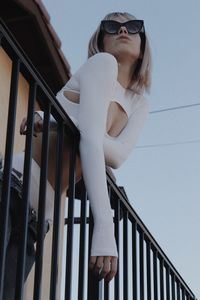 Low angle view of young woman standing against railing
