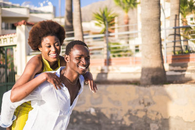 Cheerful boyfriend piggybacking girlfriend against trees