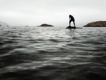 Man on rock in sea against sky