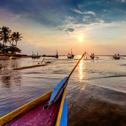 Sailboats moored on sea against sky during sunset