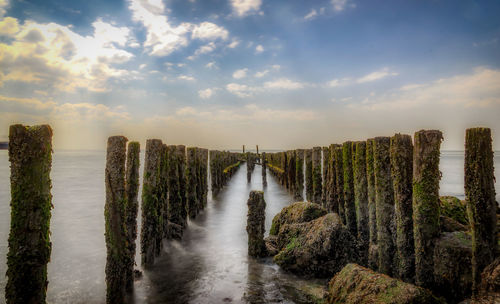 Wooden posts in sea against sky during sunset