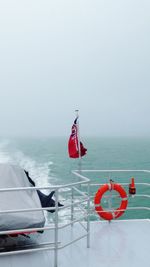 Flag on sailboat sailing in sea against sky during foggy weather