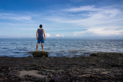 Rear view of man standing on rock at seashore against sky