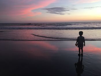 Silhouette boy standing on beach against sky during sunset