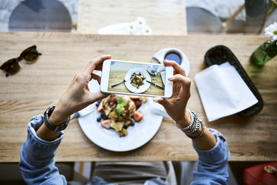 Overhead view of woman taking smartphone picture of pancakes in cafe